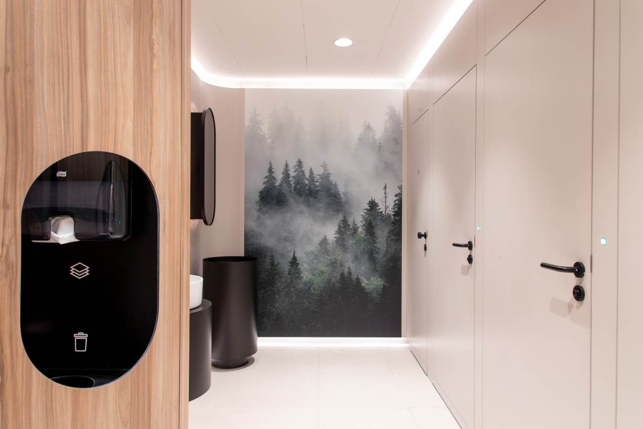 Los diseños modulares personalizables se adaptan a los diversos perfiles de usuarios. Mediante el uso de formas orgánicas y elementos inspirados en la naturaleza, estos aseos públicos ofrecen a los visitantes un entorno relajante y reparador. Su diseño combina la calidez de los materiales naturales como la piedra, la madera y las fibras texturizadas con la pulcritud y la durabilidad que requieren los espacios públicos. Los lavabos circulares e inodoros suspendidos de la colección Inspira de Roca encajan a la perfección en este ambiente, garantizando tanto la funcionalidad como la estética adecuadas. Los aseos masculinos cuentan con urinarios Chic y sistemas de descarga electrónicos Sentronic para una mayor higiene y comodidad, mientras que los aseos para personas con movilidad reducida priman la accesibilidad y el confort. Estos cuentan con asas de baño Access en un relajante acabado blanco, placas de descarga electrónica en cristal negro y espejos basculantes diseñados para adaptarse a las diferentes alturas y necesidades de los usuarios. Estos productos Roca, cuidadosamente seleccionados, permiten a cada visitante disfrutar de un momento de confort y bienestar en un espacio funcional y bien diseñado.8