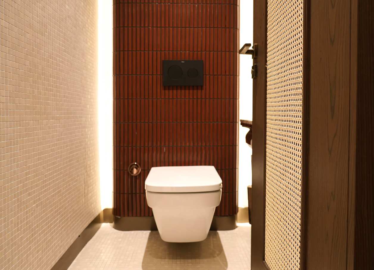 Los espacios de baño son las zonas más íntimas del restaurante y en ellos se ha optado por un diseño de líneas curvas que invita al confort. El lavabo sobre encimera de Fineceramic® Inspira Round ofrece un contrapunto orgánico a las singulares paredes curvas de los baños. La grifería electrónica de lavabo L30-E añade un plus de diseño al espacio y garantiza la eficiencia hídrica, en línea con el concepto del «Árbol de la vida». Entre los accesorios se encuentran la percha Cubica y el escobillero de pared mural Victoria, modelos minimalistas y discretos que ofrecen la máxima funcionalidad. Por otro lado, el inodoro suspendido Rimless Dama, con asiento con caída amortiguada y placa de accionamiento dual In-Wall PL10 (One), aporta un toque de modernidad y complementa el estilo acogedor y natural del espacio de baño.12