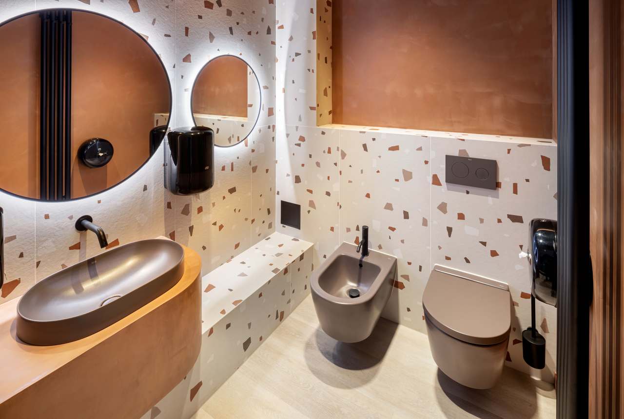 La prioridad en el diseño interior del hotel es garantizar que los huéspedes se vayan con una sonrisa, sintiéndose relajados y completamente satisfechos. Adoptando el enfoque minimalista del hygge, el diseño transmite una agradable sensación de confort a través de una cuidada selección de colores y mobiliario en materiales naturales con suaves curvas y formas orgánicas. En perfecta sintonía con la filosofía hygge, las líneas suaves y las formas redondeadas del lavabo Beyond de color café y del inodoro y bidé Inspira irradian relajación, calidez y armonía. El diseño de la colección Ona, inspirado en la naturaleza, se suma a la estética relajante. Los bidés y lavabos suspendidos contribuyen a crear una sensación de amplitud y equilibrio que evoca la serenidad de los paisajes tranquilos. De esta forma, el confort y el hygge se transmiten a todos los huéspedes del hotel. Los aseos públicos para hombres cuentan con los minimalistas urinarios Proton y los aseos accesibles están equipados con inodoros Access y asas de baño, garantizando un entorno acogedor e inclusivo para todos.14