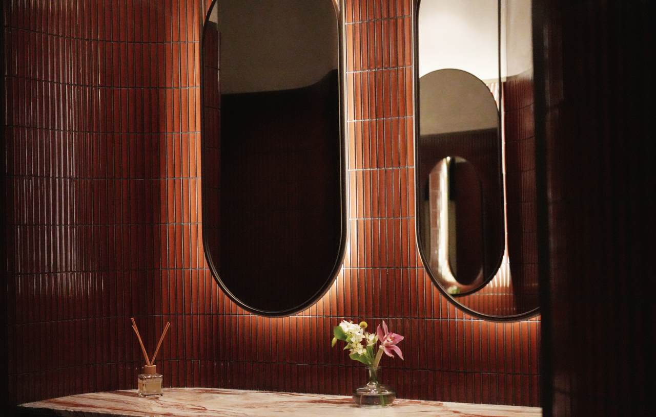 Los espacios de baño son las zonas más íntimas del restaurante y en ellos se ha optado por un diseño de líneas curvas que invita al confort. El lavabo sobre encimera de Fineceramic® Inspira Round ofrece un contrapunto orgánico a las singulares paredes curvas de los baños. La grifería electrónica de lavabo L30-E añade un plus de diseño al espacio y garantiza la eficiencia hídrica, en línea con el concepto del «Árbol de la vida». Entre los accesorios se encuentran la percha Cubica y el escobillero de pared mural Victoria, modelos minimalistas y discretos que ofrecen la máxima funcionalidad. Por otro lado, el inodoro suspendido Rimless Dama, con asiento con caída amortiguada y placa de accionamiento dual In-Wall PL10 (One), aporta un toque de modernidad y complementa el estilo acogedor y natural del espacio de baño.1