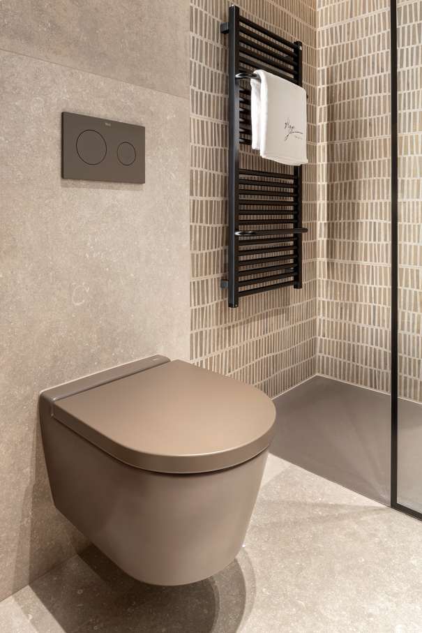 La prioridad en el diseño interior del hotel es garantizar que los huéspedes se vayan con una sonrisa, sintiéndose relajados y completamente satisfechos. Adoptando el enfoque minimalista del hygge, el diseño transmite una agradable sensación de confort a través de una cuidada selección de colores y mobiliario en materiales naturales con suaves curvas y formas orgánicas. En perfecta sintonía con la filosofía hygge, las líneas suaves y las formas redondeadas del lavabo Beyond de color café y del inodoro y bidé Inspira irradian relajación, calidez y armonía. El diseño de la colección Ona, inspirado en la naturaleza, se suma a la estética relajante. Los bidés y lavabos suspendidos contribuyen a crear una sensación de amplitud y equilibrio que evoca la serenidad de los paisajes tranquilos. De esta forma, el confort y el hygge se transmiten a todos los huéspedes del hotel. Los aseos públicos para hombres cuentan con los minimalistas urinarios Proton y los aseos accesibles están equipados con inodoros Access y asas de baño, garantizando un entorno acogedor e inclusivo para todos.9